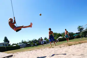 Beachvolleyball am Campingplatz: Spieler werfen den Ball in die Luft, Sandplatz und Rasenfläche im Hintergrund.