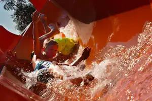 Kind und Familie spielen im Wasser in einem roten Zelt, Wasser spritzt über die Plane.