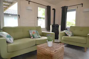 Grünes Sofa und zweites Sofa im Wohnbereich eines Mobilheims, mit Couchtisch, Kissen, Vorhängen und Fenstern.