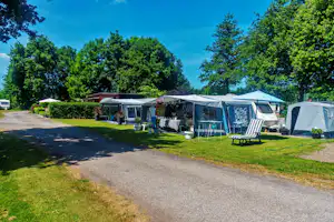 Campingzelte auf Stellplätzen im Grünen, mit Markisen, Gartenmöbeln und Bäumen entlang des Weges.
