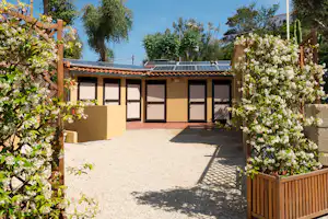 Bungalow mit Terrasse, Solarpaneelen auf dem Dach und Blumenbeeten zwischen Holzgeländern im Garten.