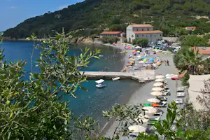 Blick auf den Strand mit Sonnenschirmen, geparkten Autos und einem weißen Gebäude am Ufer in einer geschützten Bucht.
