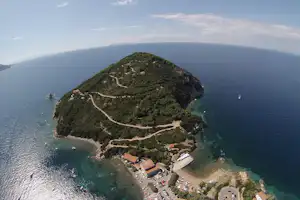 Luftaufnahme einer Insel mit Campingplatz, kleinen Buchten und Wegen, umgeben von klarem Meer und Booten.