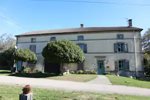 Zweistöckiges Ferienhaus mit grünen Fensterläden, gepflastertem Weg und Rasen im Vorgarten, davor Büsche und Bäume.