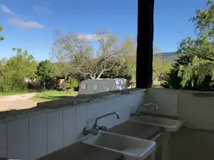 Badezimmer im Campingbereich mit Badewanne, Waschbecken und Blick auf Bäume und Wohnwagen im Hintergrund.