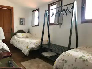 Schlafzimmer in einer Camping-Unterkunft mit zwei Betten, Bettwäsche, Nachttisch und Kleiderständer vor großen Fenstern.
