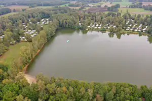 Luftaufnahme eines Sees mit Ufer im Grünen, dahinter Campingplätze mit Wohnwagen und kleinen Wegen.