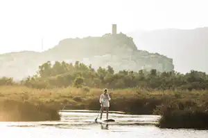 Camping Ermosa - Stand Up Paddling auf dem Fluss am Campingplatz, La Caletta auf Sardinien im Hintergrund
