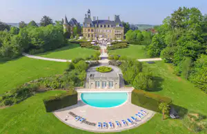 Schwimmbecken im Schlossgarten mit Liegen auf der Terrasse, gepflegtem Rasen und Blick auf das historische Gebäude.