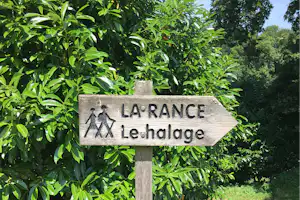 Wegweiser „LA RANCE“ mit Pfeil und Text „Le Haldage“ vor grünen Büschen und Rasen im Campingbereich.