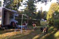 Camping et Gîtes Des Bains - Gäste sitzen vor dem Wohnmobil auf dem Wohnwagenstellplatz im Schatten der Bäume