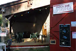 Snack-Bar „La Grange“ am Campingplatz, rote Holzwand, Tische und Stühle unter dem überdachten Bereich.