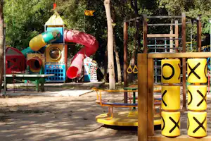 Spielbereich mit gelben Buchstaben-Sitzhockern und Wasserbahn, im Hintergrund bunte Spielgeräte im Grünen.