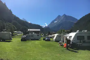 Campingplatz mit Wohnmobilen und Wohnwagen auf einer Wiese, umgeben von Bergen und Tannen im Tal.
