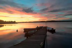 Steg am See mit zwei Booten, Holzplanken und ruhigem Wasser bei Sonnenuntergang.