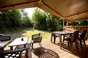 Holzterrasse mit Tisch und Stühlen am Wohnwagen-Stellplatz, Blick in den Garten mit Wegen und Bäumen.
