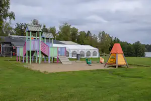 Buntes Spielhaus auf dem Campingplatz, daneben Zelte mit Fenstern und ein gelbes Spielzelt im Grünen.