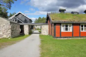 Holzhäuser und Ferienunterkünfte auf einem Campingplatz, mit Kiesweg, Rasen und Steinmauer zwischen den Gebäuden.