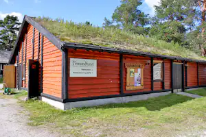 Gebäude von Femundtunet mit Holzfassade, Eingang und Schildern für Hotel und Restaurant, neben Rasen und Bäumen.