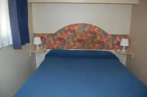 Bett mit gepolstertem Kopfteil und zwei Nachttischen mit Lampen in einem Campingzimmer.
