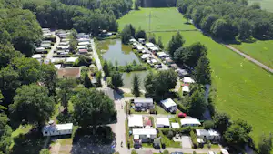 Campingplatz am Fluss mit vielen Stellplätzen, Wohnwagen und Bäumen, umgeben von grünen Wiesen und Wegen.