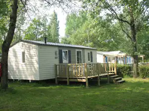 Mehrere Mobilheime auf einem Campingplatz, mit Holzveranda, Rasenfläche und Bäumen im Hintergrund.