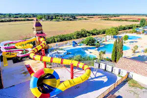 Bunte Wasserrutschen und ein Pool auf dem Campingplatz, mit Liegen, Beckenrand und Blick über die Landschaft.