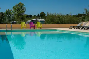 Blauer Camping-Pool mit Liegen und bunten Stühlen am Beckenrand, im Hintergrund Bäume und ein Zaun.
