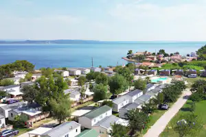 Campinganlage am Meer mit Wohnwagen und Mobilheimen, gepflastertem Weg, Bäumen und Blick auf die Küste.