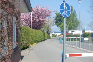 Campingplatz-Weg mit Hecke, Zeltwand links und blauem Schild für Fußgänger und Fahrradfahrer.