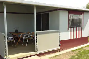 Terrasse am Wohnwagen mit Tisch und Stühlen, Markise und großen Fenstern mit Vorhängen.