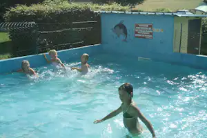 Kinder im Schwimmbecken mit Spritzwasser, im Hintergrund Zaun und Beschilderung an der Poolwand.