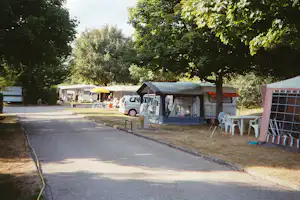 Wohnwagen mit Vorzelt und Campingstühlen am Stellplatz, daneben ein weiterer Camper unter Bäumen am Campingplatz.