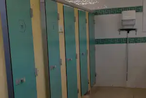Camping-Badezimmer mit türlosen Duschkabinen, türkisfarbenen Türen und Fliesenwand, oben eine Duschbrause.
