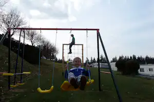 Klettergerüst auf dem Campingplatz mit Seilen, Netz und Rutsche, im Hintergrund Wohnwagen und Bäume.