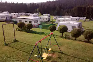Wohnwagen und Campingbusse auf dem Stellplatz, Blick über Rasen mit Hecken und Spielgerüst im Vordergrund.