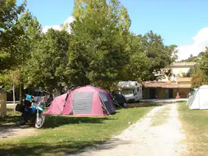 Rosa Zelt auf einem Campingplatz am Grasweg, daneben Motorrad und Wohnwagen, Bäume und Hecken im Hintergrund.