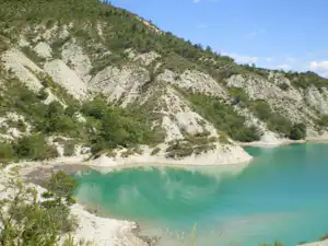 Türkisfarbenes Wasser in einer Bucht vor steilen, bewaldeten Felswänden und einem Kiesstrand am Ufer.