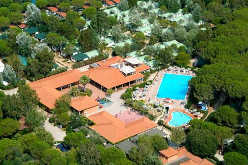 Luftaufnahme eines Campingplatzes mit zwei Pools, roten Dächern, Terrassen und Wegen zwischen Bäumen und Grünflächen.