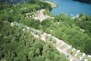 Luftaufnahme eines Campingplatzes am Fluss mit Stellplätzen, Wegen und Booten im Wasser, umgeben von viel Grün.