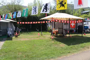 Campingplatz mit mehreren Zelten, Wimpelketten und einem Pavillon mit Stühlen und Tisch im Garten.