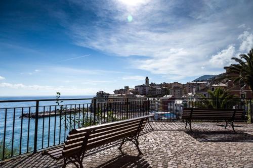 Terrasse mit Bank und Geländer, Blick aufs Meer und auf einen Küstenort mit Häusern und Palmen.