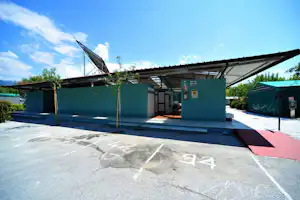 Waschhaus am Campingplatz mit Duschen, grünen Wänden und Eingang, davor Stellplätze mit Markierungen und Sonnenschirm.