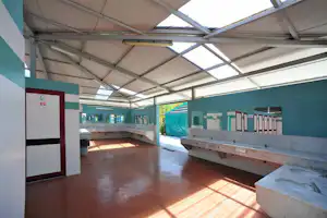 Überdachter Sanitärbereich mit Waschbecken, Spülbecken und Toiletten, Ziegelboden und grünen Wänden im Campingplatzgebäude.