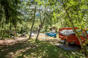 Campingplatz im Grünen: Wohnmobil mit Vorzelt, Hängematte und Zelt zwischen Bäumen, daneben Autos und ein Weg.