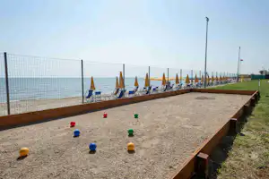 Boulebahn am Campingplatz mit bunten Kugeln, Holzrand und Blick auf das Meer, daneben Sitzbereich und Zaun.