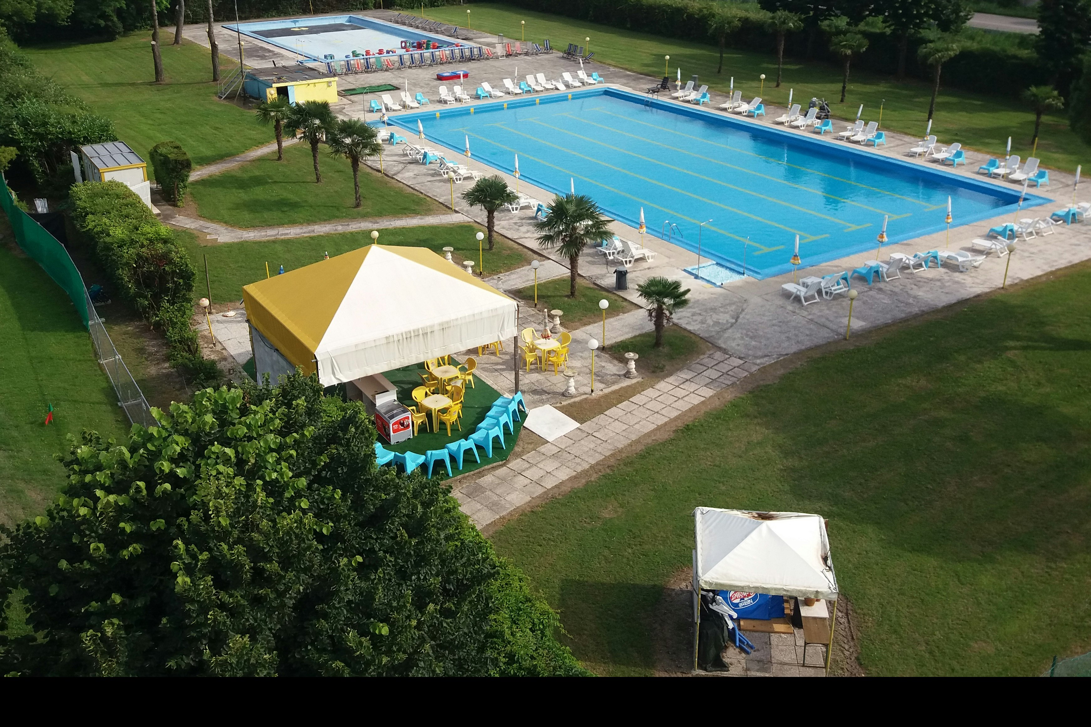 Großes Schwimmbecken mit Liegen und Sonnenschirmen, daneben ein Zelt und Wege im gepflegten Campingbereich mit Bäumen.
