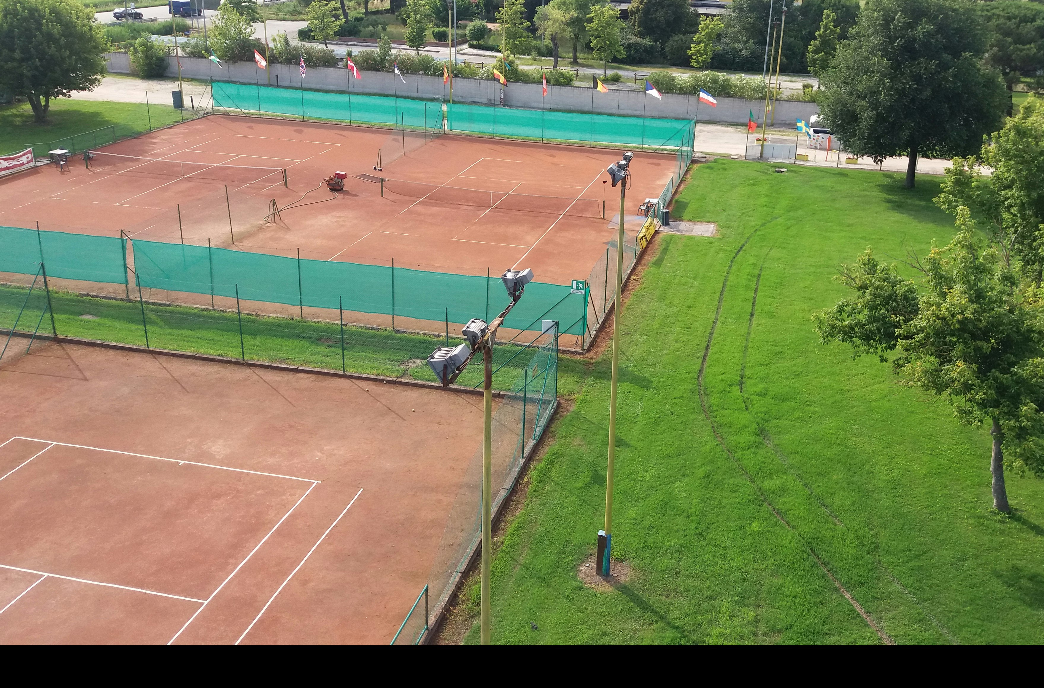 Blick auf einen Tennisplatz mit Umzäunung und Netzen, daneben ein großer Pool und gepflegte Rasenflächen im Campingbereich.