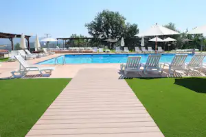 Schwimmbad mit blauem Wasser, Liegen auf Holzterrasse und Rasenfläche, daneben weiße Sonnenschirme und Zelte im Hintergrund.