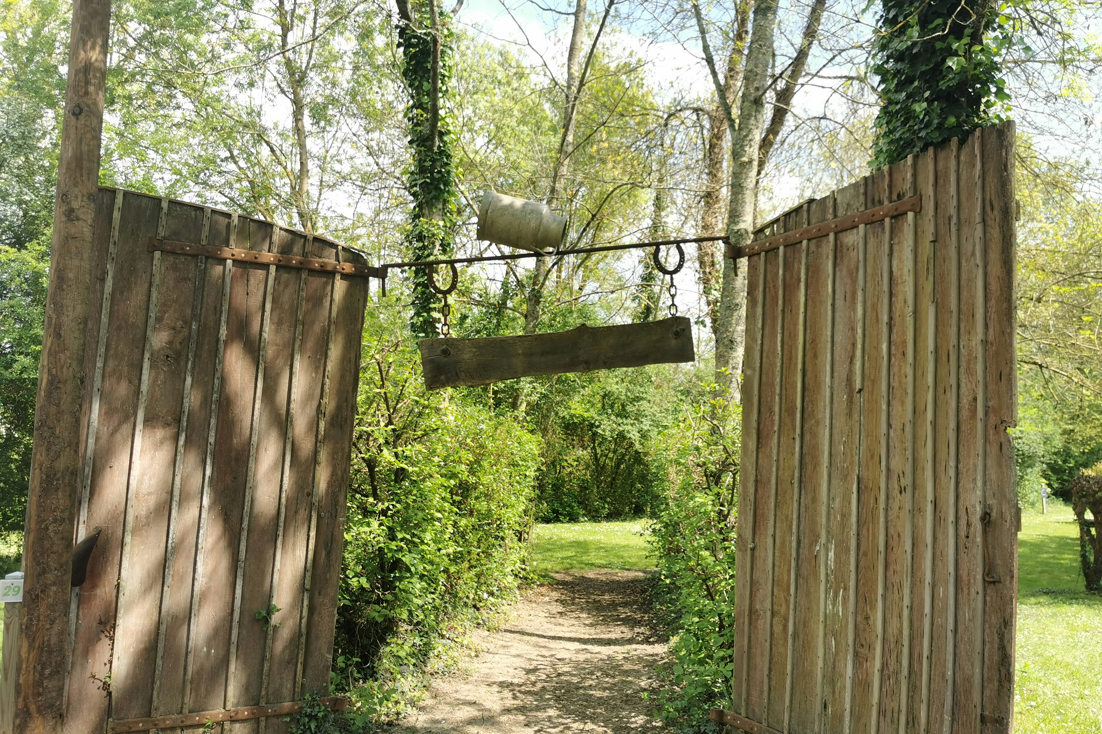 Holzlattenzaun und schmaler Weg im Grünen, umgeben von Bäumen und Sträuchern auf einem Campingplatz.